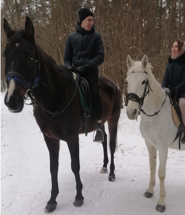Фотография пары на лошадях в лесу. Молодой человек сидит на тёмно-гнедой лошади, девушка на белой (серой). Они смотрят друг на друга. На лицах выражения положительных эмоций.