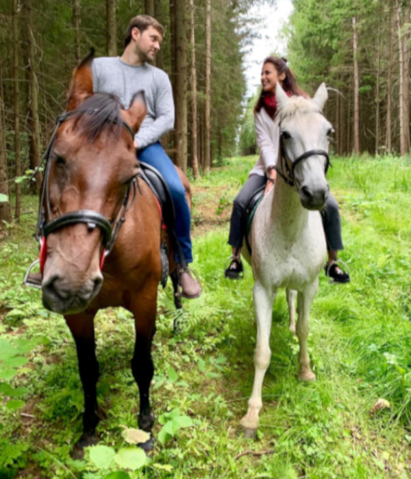 Фотография пары на лошадях в лесу. Молодой человек сидит на тёмно-гнедой лошади, девушка- на белой(серой).